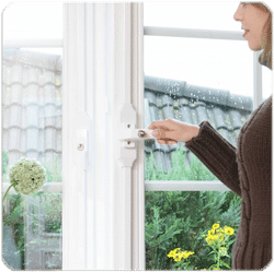 Auf dem Bild ist eine Frau mittleren Alters zu sehen, die ein Fenster öffnet. Dieses Fenster ist mit einem Fensterstangenverschluss abgesichert.
